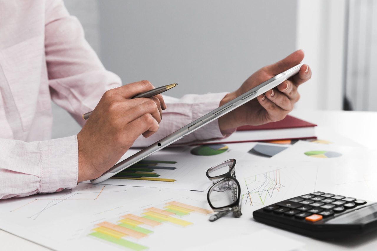 Homem com tablet, caneta, óculo, calculadora e cálculos do Imposto de Renda 2024 