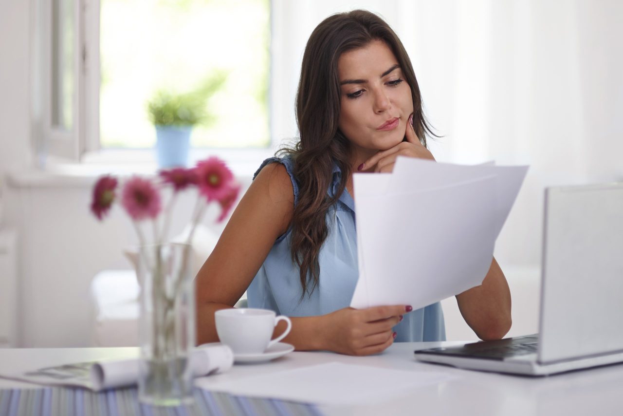Mulher sentada em mesa com computador e xícara de café com documentos de imposto de renda
