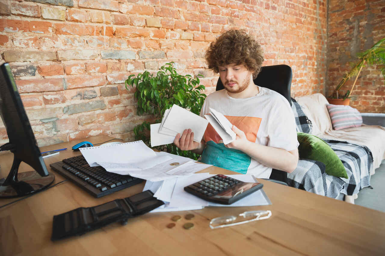 Homem sentado em escritório com papéis, computadores e calculadora do imposto de renda