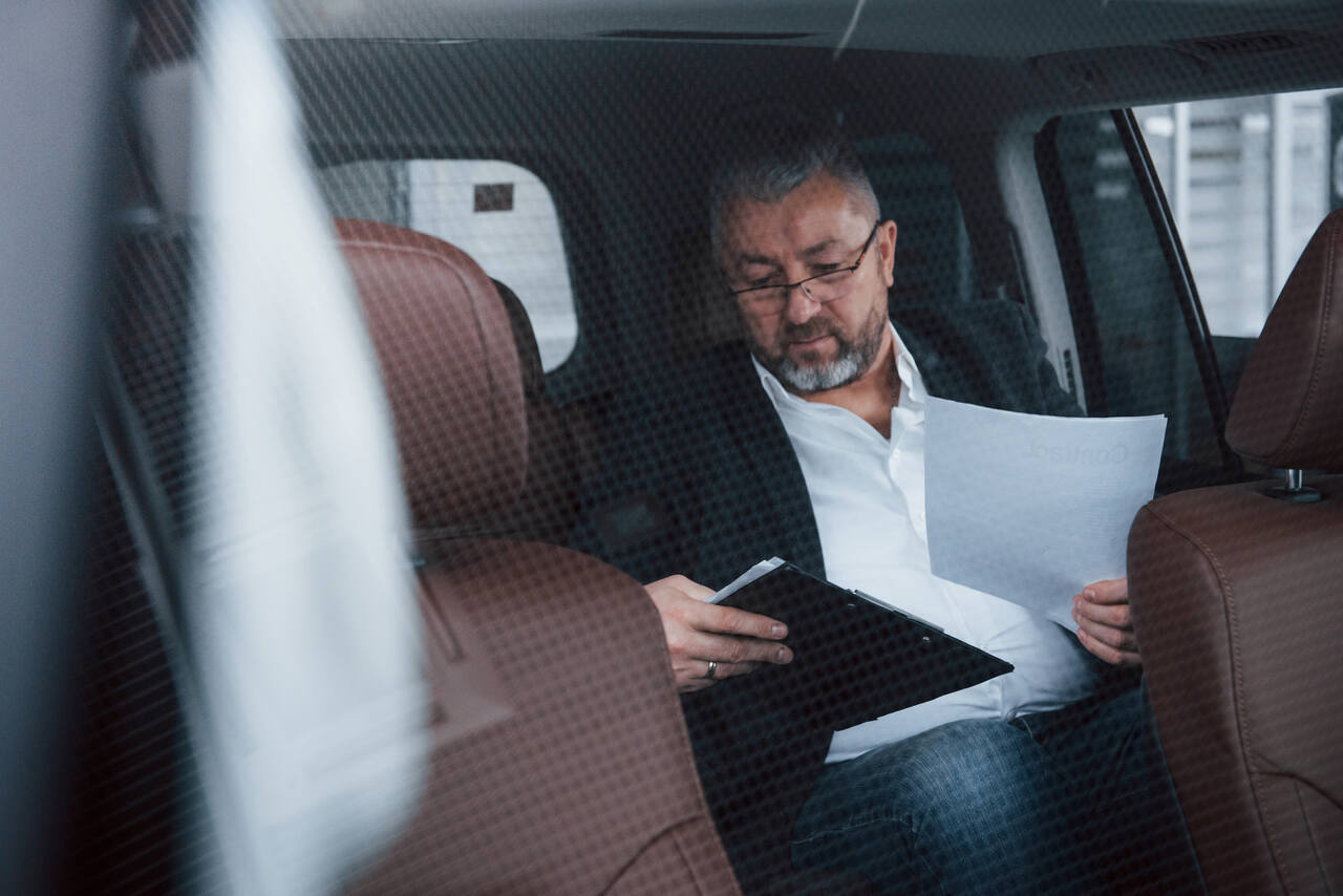 Homem sentado em carro com papéis do imposto de renda 2024 